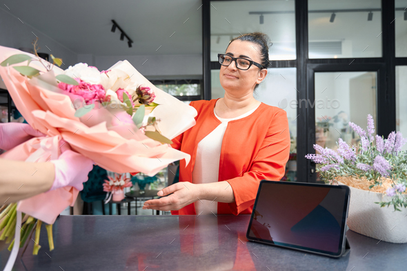 Woman client receives ordered bouquet of flowers in flower shop