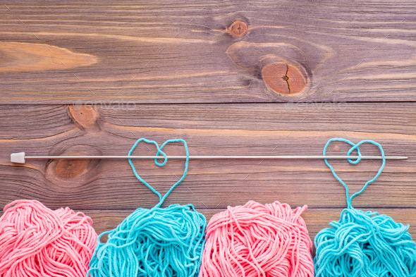 Tangles of pink and mint yarn, hearts with needle on a wooden background. Top view