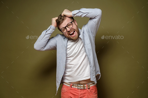 Caucasian man in stress, he is trying to tear his hair out and looks crazy, on a green background.