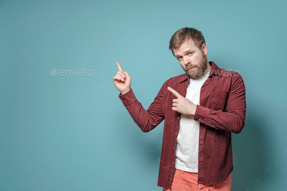 Calm, beautiful bearded man in a burgundy, velveteen shirt, insists with index finger on copy space