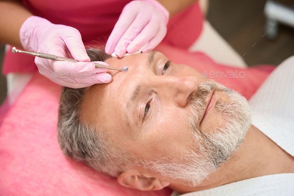 Cosmetologist with spoon uno clean face of man from acne - Stock Photo - Images
