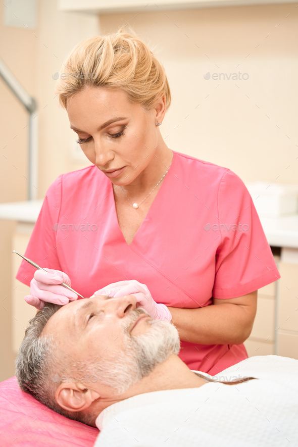 Attractive woman beautician with uno spoon cleans man face - Stock Photo - Images