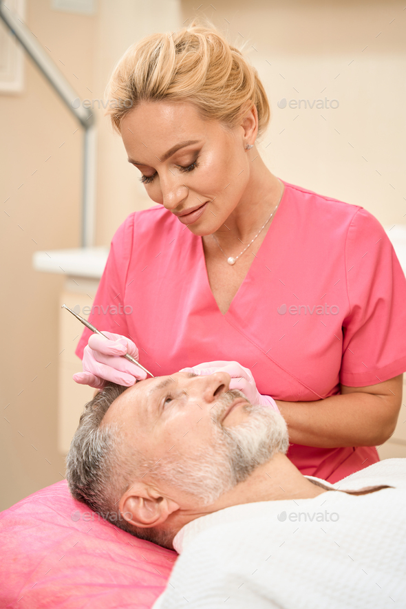 Focused female beautician with uno spoon cleans man face - Stock Photo - Images