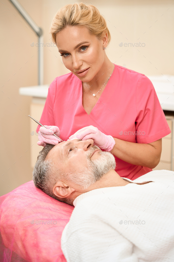 Smiling woman beautician with uno spoon cleans man face - Stock Photo - Images
