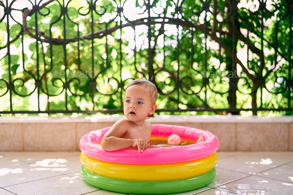 Cute baby sits in inflatable mini pool, turning back