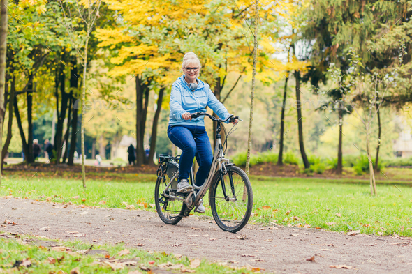 Senior beautiful blonde woman rides a bike in the park, in the woods, in nature, listens to music