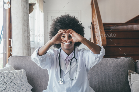Woman physician doing heart shape gesture with hands. Smiling black female doctor making a love