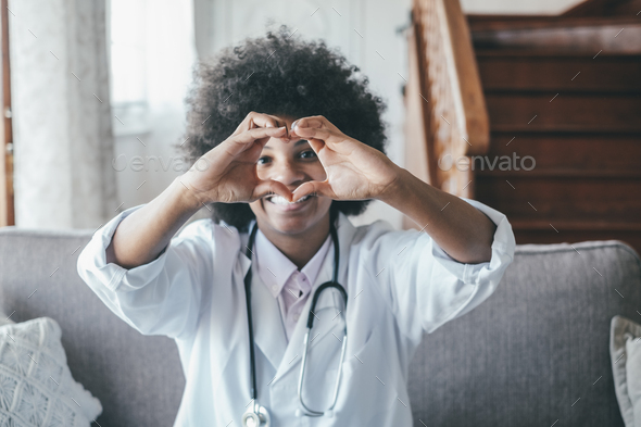 Woman physician doing heart shape gesture with hands. Smiling black female doctor making a love