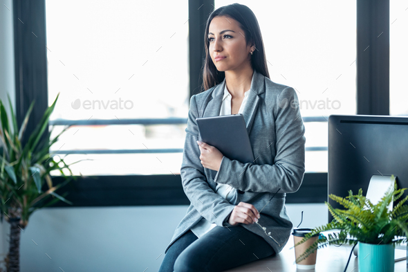 Beauty business woman using her digital tablet while sitting on a desk in a modern startup office. - Stock Photo - Images
