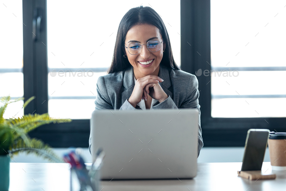 Confident business woman looking and speaking through the webcam while making a video conference - Stock Photo - Images