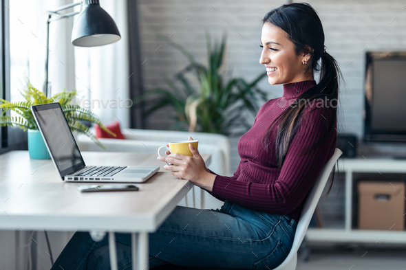 Concentrated young business woman working with computer while drinking coffee in the office at home. - Stock Photo - Images