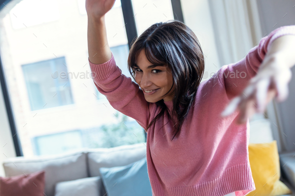 Pretty young woman listening to music while dancing in the living room at home. - Stock Photo - Images