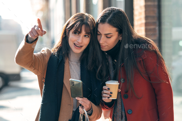 Two beuatiful tourist friends consulting an online guide on a smart phone in the street. - Stock Photo - Images