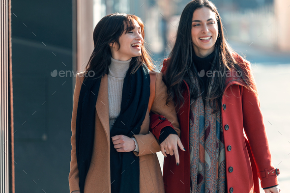 Two beautiful friends talking and having fun while walking on the city street with shopping bag. - Stock Photo - Images