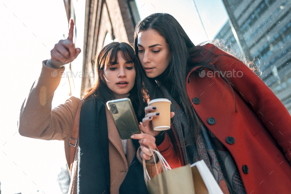 Two beuatiful tourist friends consulting an online guide on a smart phone in the street. - Stock Photo - Images