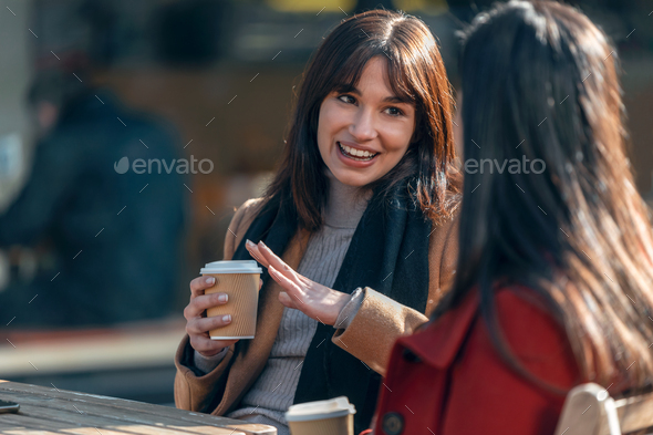 Two attractive friends enjoying coffee together while talking and laughing sitting on a terrace - Stock Photo - Images