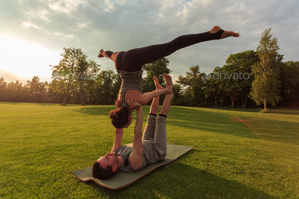 Healthy man lying on grass and balancing woman. Couple doing acrobatic ...