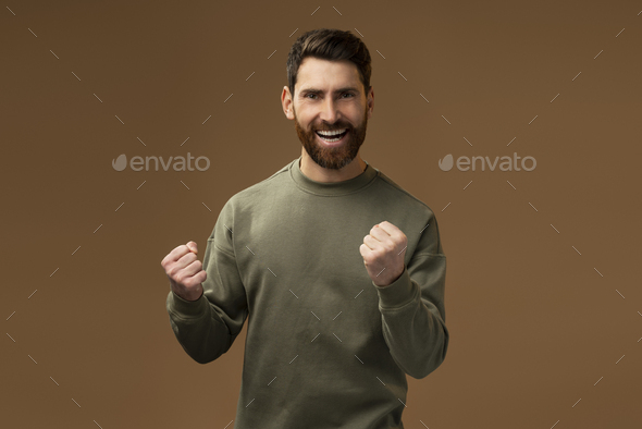 Portrait of ecstatic brunette man with beard showing yes i did it gesture and rejoicing