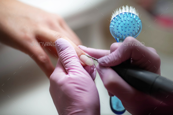 Woman uses electric nail file drill in beauty salon. Close up of nail manicure process.