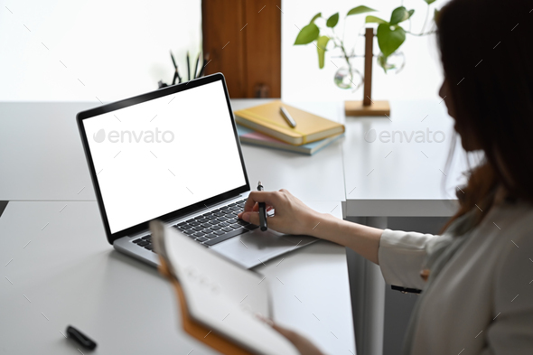 View over shoulder businesswoman holding notebook and using laptop at her office desk.
