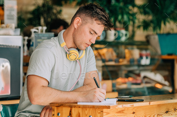 Stylish male studen sits at table in a cafe with pen and notebook