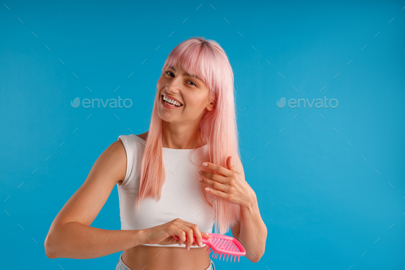 Cheerful woman brushing her smooth natural long pink hair with hair comb while posing isolated over