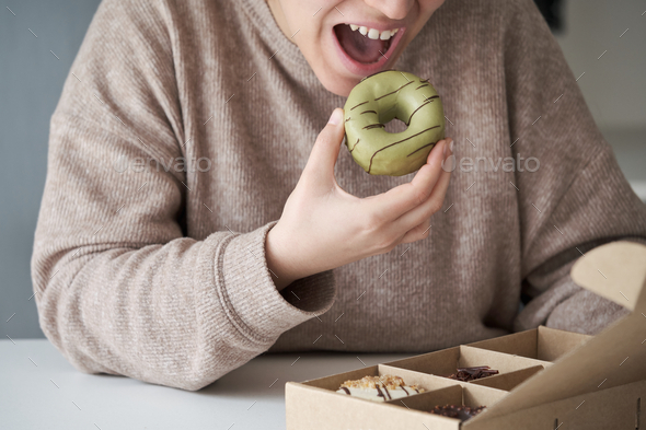 Unrecognizable woman eating matcha donut from crafted donuts takeaway box.