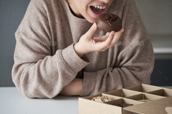 Unrecognizable woman eating chocolate donut from crafted donuts takeaway box.