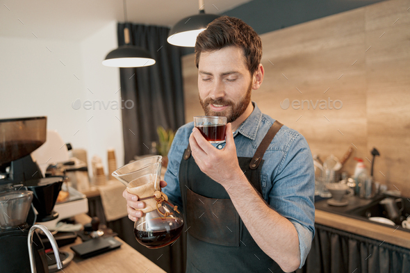 Handsome barista with stylish beard smelling filter coffee in cafeteria ...