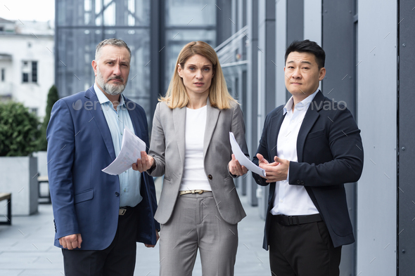 Frustrated female business boss with documents looking at camera, team of diverse colleagues outside