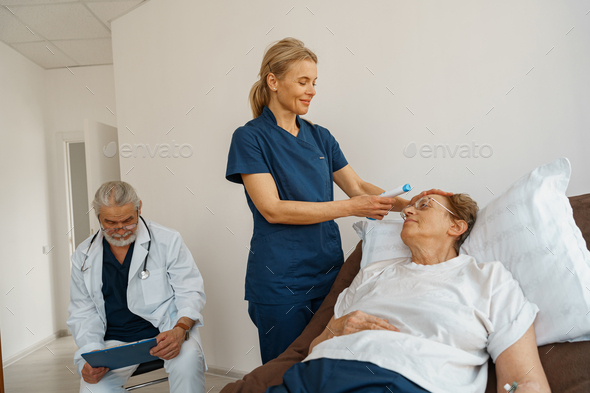 Doctor measures patient\'s temperature with non-contact thermometer in hospital ward