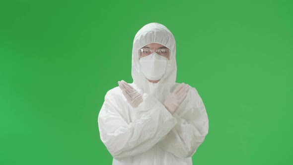 Asian Man Wear Protective Uniform PPE, Medical Face Mask And Show Stop Sign In Green Screen Studio alt