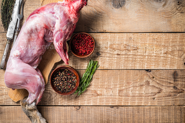 Raw Whole wild hare, fresh game meat on wooden board with herb. Wooden background