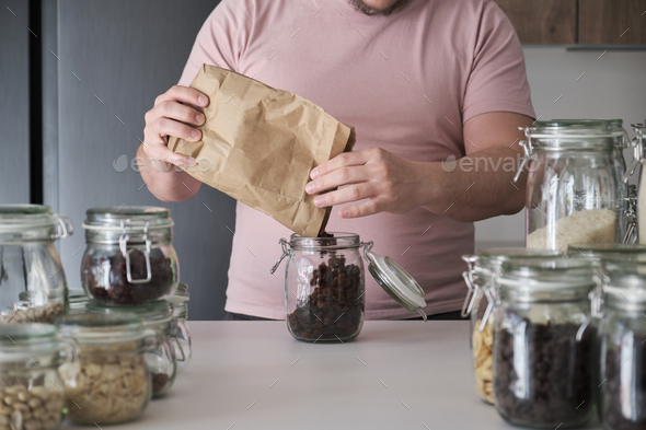 Unrecognizable latin man filling up a jar with raisins from a paper bag.
