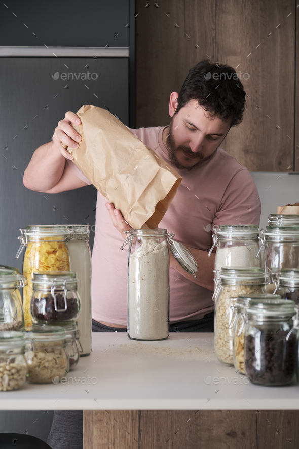 Young latin man filling up a jar with whole wheat flour from a paper bag.