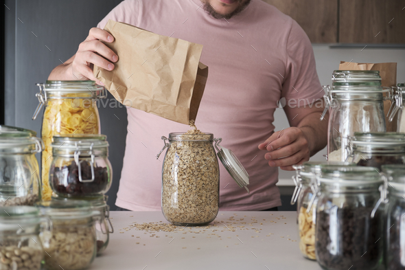 Unrecognizable latin man filling up a jar with oat flakes from a paper bag.