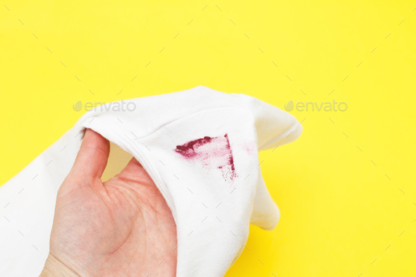female hand holding white shirt with red lipstick stain on yellow background