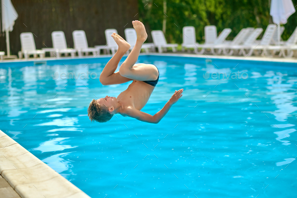 Boy in air upside down above pool water