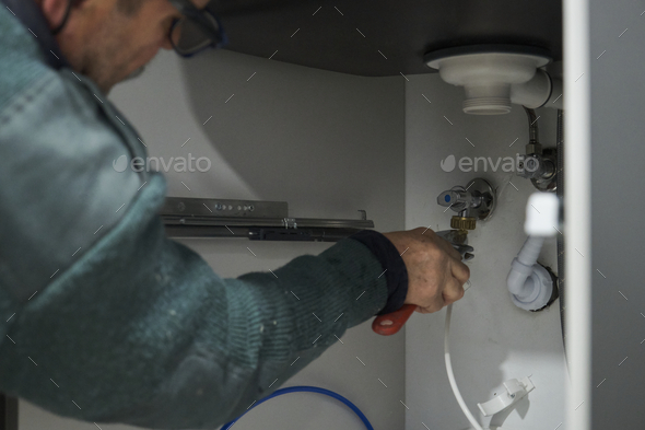 Mature technician connecting water to american fridge using a wrench.