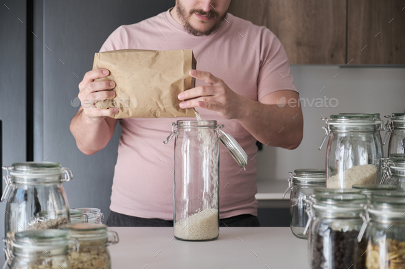 Unrecognizable latin man filling up a jar with round grain rice from paper bag.