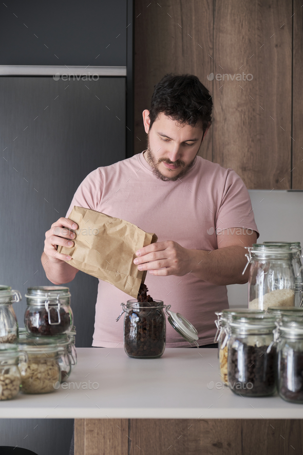 Young latin man filling up a jar with raisins from a paper bag.