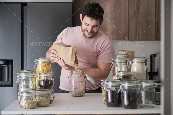 Young latin man filling up a jar with oat flakes from a paper bag.