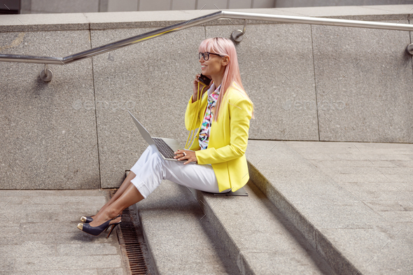 Female with pink hair speaking on phone using laptop