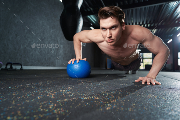 Shirtless muscular man performing press-up on gym floor