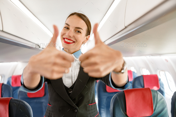 Joyful woman flight attendant doing thumbs up gesture in airplane Stock ...