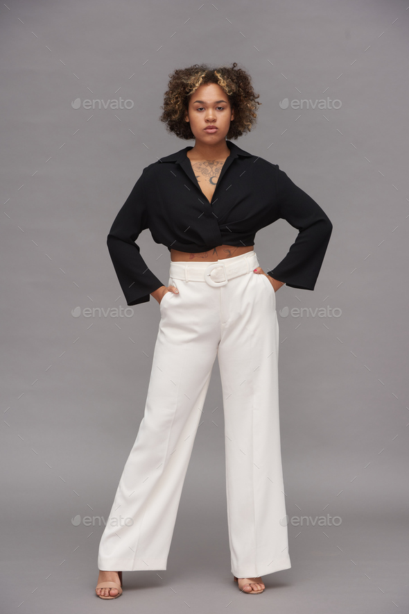 Young confident multi-ethnic woman in black cropped top and white pants