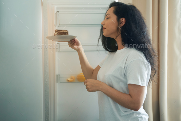 Young female is putting dessert in fridge