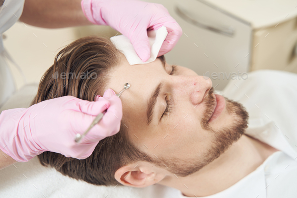 Beauty worker pressing uno spoon to man forehead - Stock Photo - Images