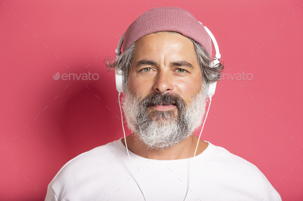Close up of handsome grey-bearded man in earphones listening to music or talking on mobile phone