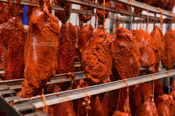pieces of pork delicacies in paprika and spices are hung on a metal rack in a meat-packing plant or